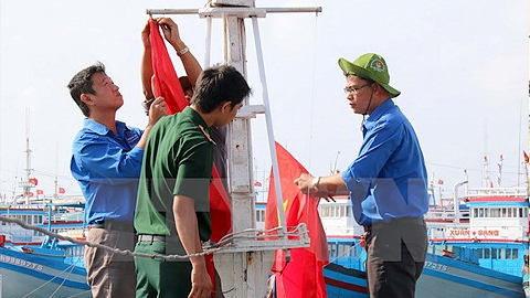 Các đoàn viên giúp ngư dân treo cờ Tổ quốc lên tàu cá. (Ảnh: Nguyễn Thanh/TTXVN)