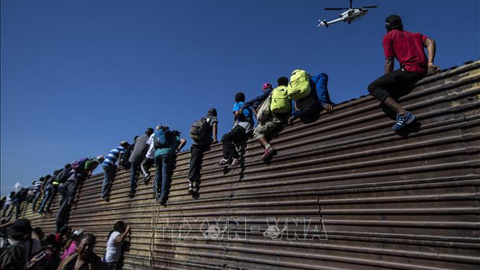 Người di cư vượt qua bức tường biên giới Mỹ - Mexico ở gần cửa khẩu El Chaparral, Tijuana, bang Baja California, Mexico ngày 25-11-2018.  Ảnh: AFP/TTXVN