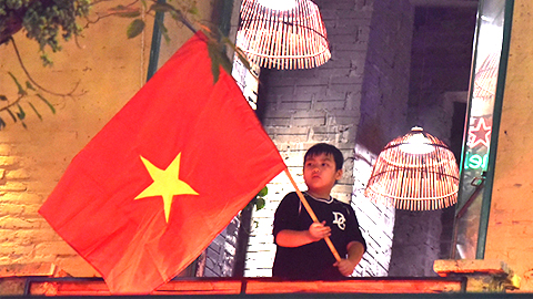 Một cậu bé đứng vẫy cờ chào đón đoàn người ăn mừng trên phố Bà Triệu.