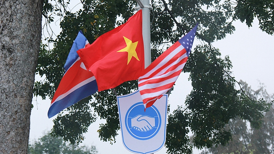 Bên dưới cờ 3 nước là biểu tượng hai bàn tay bắt chặt thể hiện tinh thần hòa bình của Hội nghị Thượng đỉnh giữa Hòa Kỳ và Triều Tiên. 