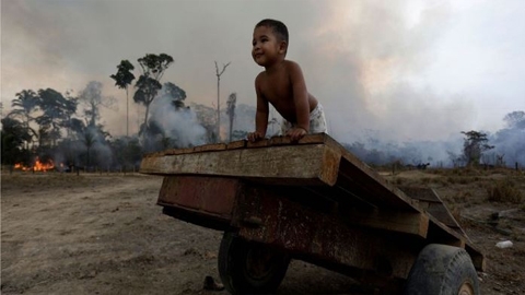Cậu bé Jose (2 tuổi) vui chơi trong khi một khu rừng cháy nghi ngút. Nguồn: Reuters