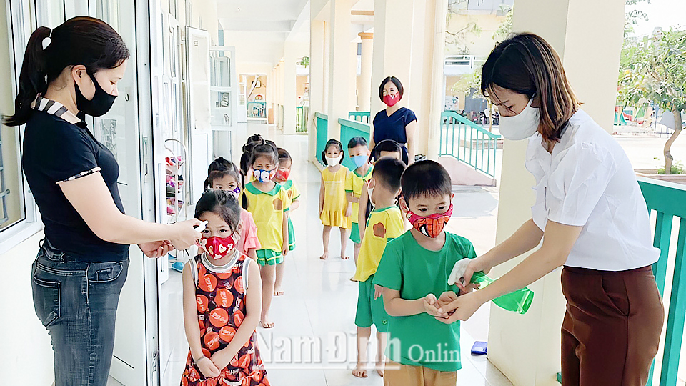 Giáo viên Trường Mầm non thị trấn Nam Giang (Nam Trực) đo thân nhiệt và hướng dẫn trẻ sát khuẩn tay trước khi vào lớp.