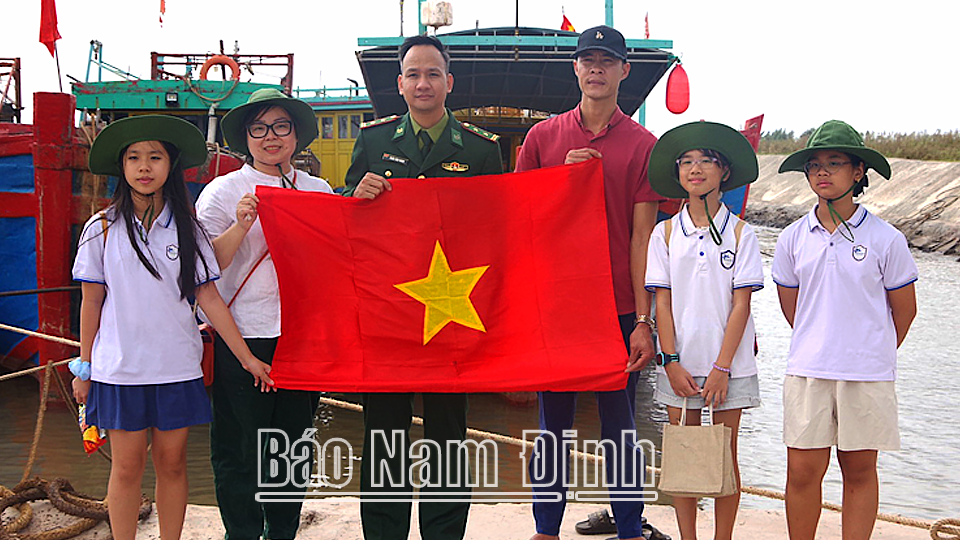 Cán bộ, chiến sĩ Đồn Biên phòng Ba Lạt (Giao Thủy) và các em học sinh trường Tiểu học Ban Mai, quận Tây Hồ (Hà Nội) tặng Cờ Tổ quốc cho ngư dân.