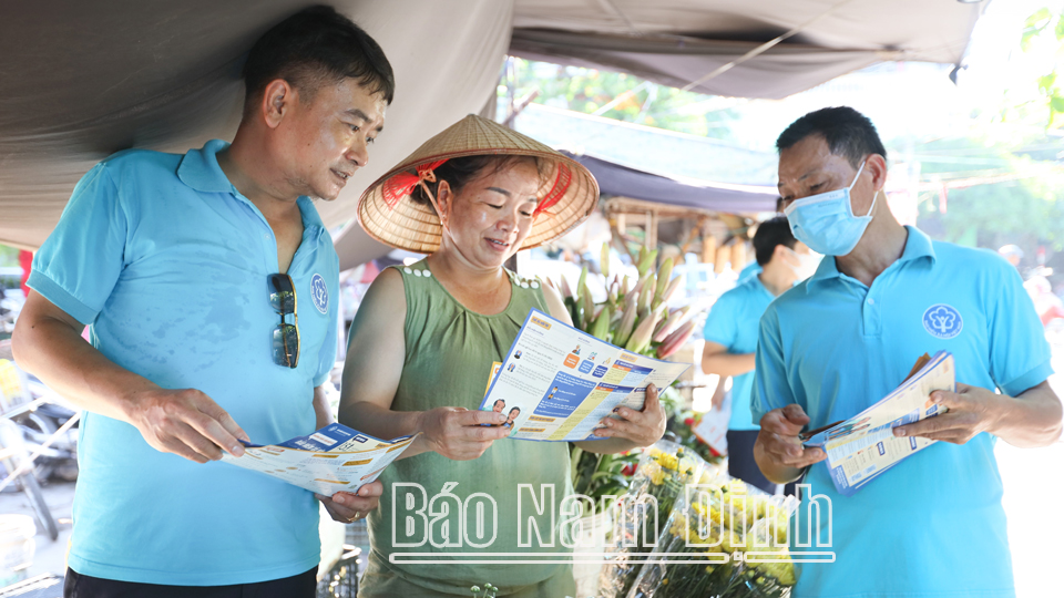 Cán bộ Bảo hiểm xã hội tỉnh tư vấn cho người dân về chính sách bảo hiểm y tế tại chợ Hạ Long (thành phố Nam Định).