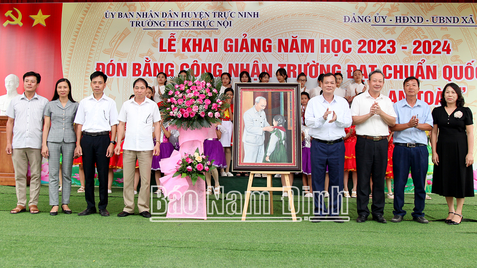 Đồng chí Phó Bí thư Thường trực Tỉnh ủy Lê Quốc Chỉnh trao tặng bức tranh “Bác Hồ đeo khăn quàng cho cháu thiếu nhi” và lẵng hoa tươi thắm chúc mừng thành tích của trường THCS Trực Nội (Trực Ninh).