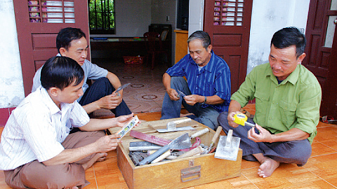 Ông Đỗ Ngọc Quyển và ông Lê Văn Biền (bên phải ảnh) lần giở những kỷ vật là chiếc bàn xoa, dao xây, bay, thước dây… đã cùng các ông xây dựng ở Trường Sa.