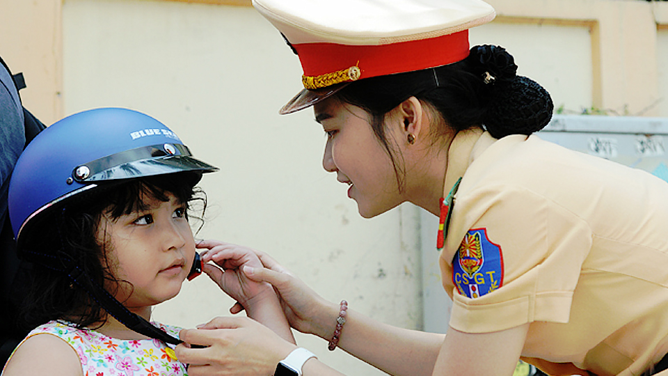 Cán bộ Phòng CSGT tặng mũ bảo hiểm cho trẻ em và hướng dẫn cách đội mũ bảo hiểm an toàn. 